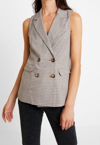 Dubbelt knäppt väst i rutigt mönster; har en slagkrage, två framfickor, guldtonade knappar och en figursydd design.