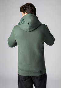 Grüne Kapuzenjacke aus weichem Stoff, mit einer großen Kapuze, gerippten Bündchen und einem Logo-Druck auf dem Rücken und dem Ärmel. Einfaches Design, lässiger Schnitt.