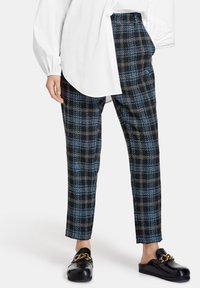 Zwarte en blauwe geruite tailleurbroek met een relaxte pasvorm, gemaakt van gestructureerde stof. Gecombineerd met zwarte instapschoenen met een gouden ketting.