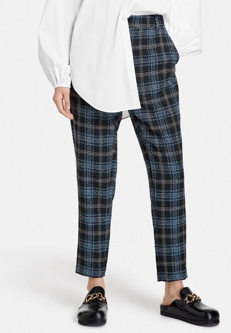 Zwarte en blauwe geruite tailleurbroek met een relaxte pasvorm, gemaakt van gestructureerde stof. Gecombineerd met zwarte instapschoenen met een gouden ketting.