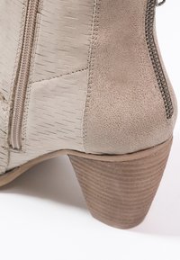 Bottine beige en cuir texturé, fermeture éclair latérale et talon bloc en bois empilé sur fond blanc.
