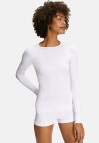 White long-sleeve top with a rounded neckline, featuring textured paneling on sleeves and a fitted silhouette. Accompanied by matching shorts.