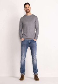 Grijze ronde hals trui, lichtblauwe slim-fit jeans en bruine veterschoenen. De jeans zijn iets versleten en de trui heeft een gladde textuur.