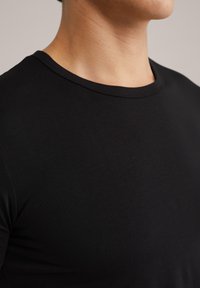 T-shirt noir ajusté avec un col rond, texture lisse et manches courtes, montrant un gros plan de la zone supérieure du corps.