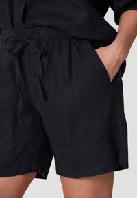 Bermudas de lino azul oscuro con cinturilla ajustable, bolsillos laterales y un corte relajado. La tela presenta una sutil textura y un aspecto ligero.