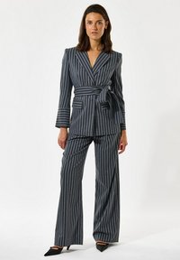 Navy pinstripe-puku sisältää kietaisupuvun, jossa on sidottu vyötärö ja leveälahkeiset housut, joilla on sileä pinta ja terävät läpät.