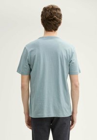 Tricou scurt, cu mânecă scurtă, de culoare albastru deschis, cu guler rotund, confecționat dintr-un material moale. Design simplu, fără modele sau accente vizibile.