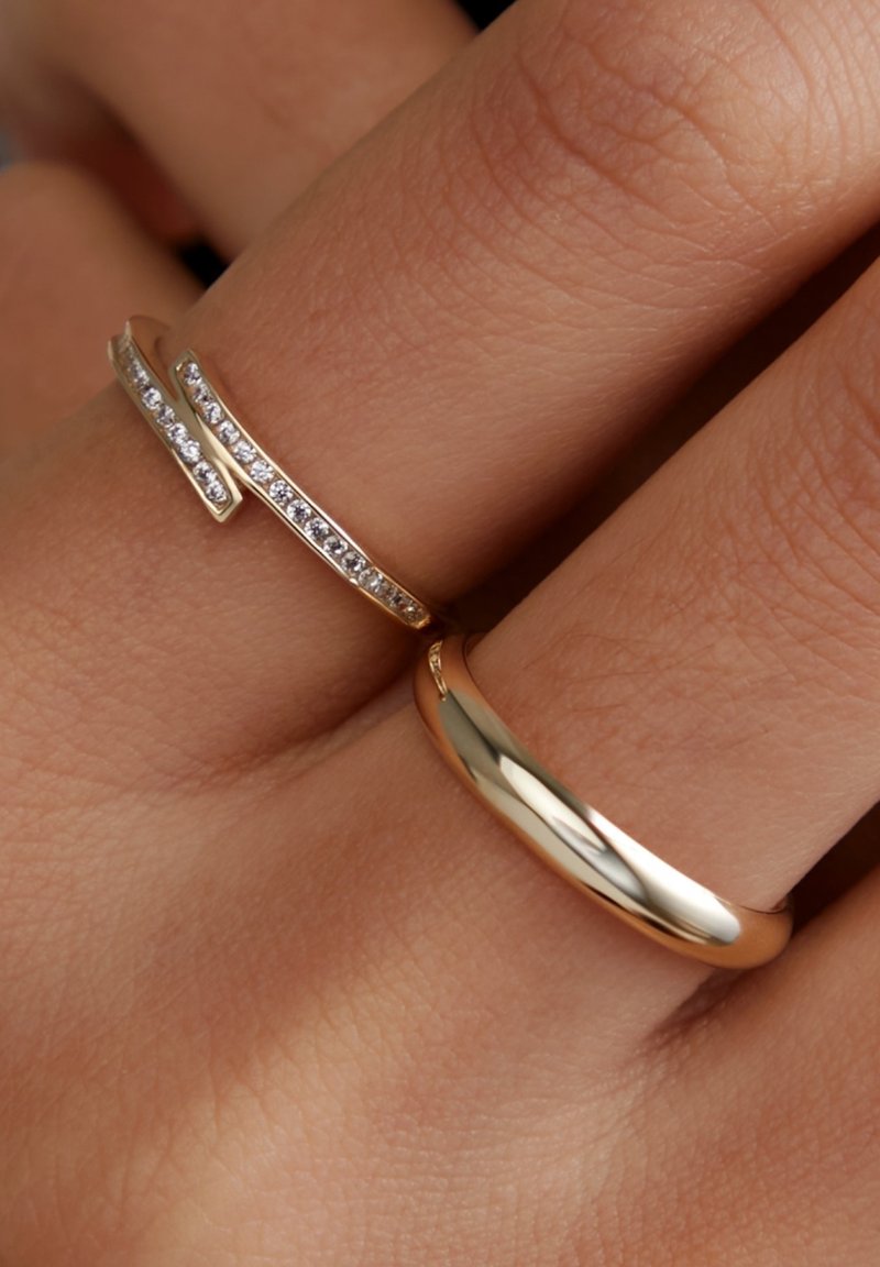 Zwei Ringe an einer Hand: ein goldener Ring mit glatter Oberfläche und ein schlanker goldener Ring mit einer Reihe funkelnder Edelsteine.