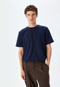 Mørkeblå kortærmet t-shirt lavet af blødt stof, med rund hals og afslappet pasform, parret med brune skræddersyede bukser.