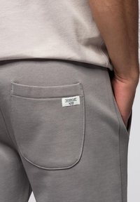 Grijze sweatpants van een textuur gemaakt van zacht materiaal. Heeft een enkele achterzak en een klein merkembleem bevestigd.