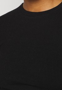 Svart ribbad t-shirt med rund hals och strukturerad tyg. Närbild som framhäver texturen och färgkonsistensen.