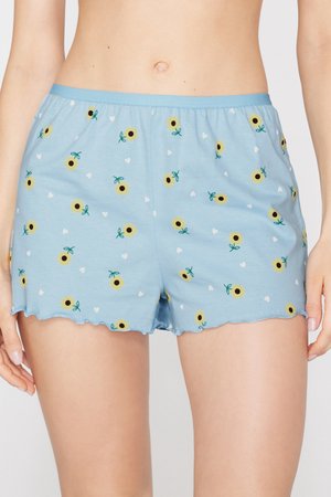 Pantalones cortos azul claro con estampados de girasoles y pequeños corazones blancos, usados por una persona que muestra la zona media y la parte superior de los muslos.