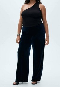 Mustat ribbimekko yhdistettynä tummansinisiin samettisiin leveälahkeisiin housuihin. Mallilla on jalassaan matalat sandaalit ja hopeinen koru yhdessä ranteessa.