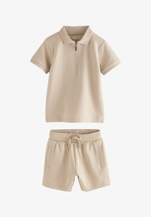 Camisa polo de manga corta beige con cremallera en el frente y pantalones cortos con cordón a juego en beige, con bolsillos laterales.
