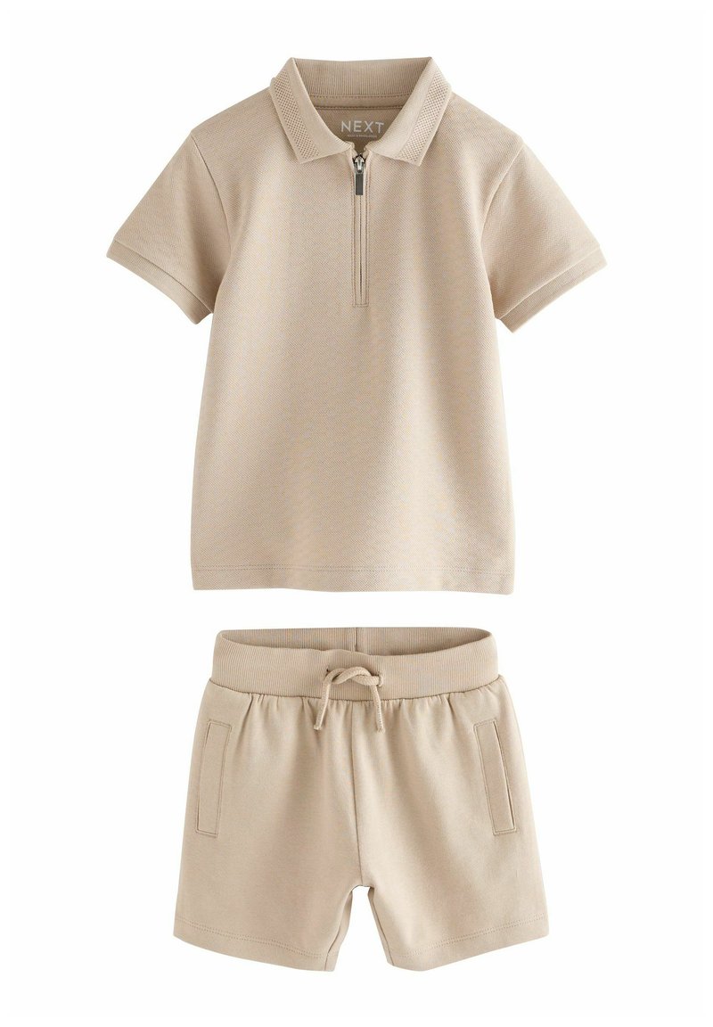 Polo shirt beige à manches courtes avec une fermeture éclair à l'avant et un short beige avec cordon de serrage assorti et poches latérales.