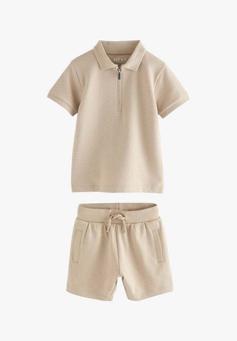 Beżowa koszulka polo z krótkim rękawem z zamkiem błyskawicznym z przodu oraz dopasowane beżowe szorty z gumką w talii i bocznymi kieszeniami.