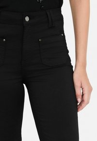 Musthave mustad kõrge vöökoha ja kahe esisegmendiga, metallnupuga ja õmblusdetailidega. Kude on sile ja kitsas lõige.
