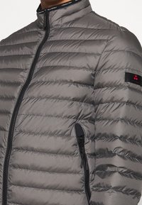 Veste grise rembourrée avec un col haut, présentant des coutures horizontales, une fermeture éclair à l'avant et une poche latérale avec des accents en métal noir.