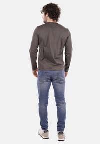 Koszula z długim rękawem w ciemnoszarym kolorze, wykonana z miękkiego materiału, w połączeniu z niebieskimi dżinsami. Koszula ma okrągły dekolt i luźny krój.