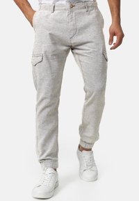 Helle graue Cargo-Hosen aus strukturierter Stoff, mit Seitentaschen, elastischen Bündchen und einem Knopfverschluss. Kombiniert mit weißen Sneakers.