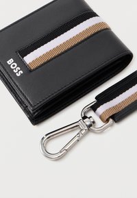 Juodas odinis piniginė su tekstūruota paviršiumi, turinti rudą ir baltą dryžuotą akcentą. Įeina sidabrinis metalinis užtrauktukas ir dirželis.