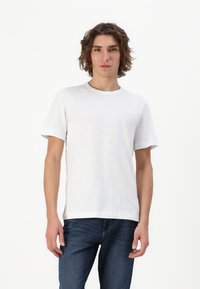 Hvid kortærmet T-shirt lavet af blødt, let materiale med rund halsudskæring. Modellen parrer den med blå jeans og står foran en hvid baggrund.