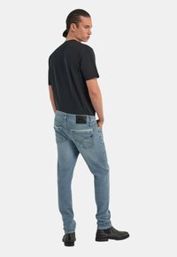 T-shirt nera a maniche corte abbinata a jeans chiari strappati con etichetta nera sul taschino posteriore e stivali neri alla caviglia.