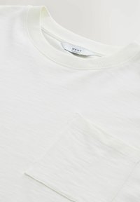 T-shirt blanc à coupe décontractée avec un col côtelé et une poche plaquée sur la poitrine gauche. Tissu doux, texturé avec une finition subtile.