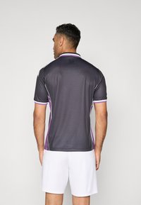 Polo deportivo gris con acentos morados, de mangas cortas y cuello. Hecho de un material suave y transpirable con un acabado texturizado.