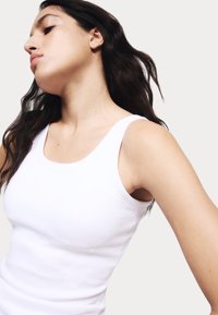 Witte tanktop met een getailleerd ontwerp, gemaakt van ribbelstof. Beschikt over brede schouderbanden en een ronde halslijn. Soepele textuur.