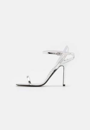 Hõbedased kõrged kontsad õhukeste rihmadega ja stiilse disainiga. Omab teravat nina ja stiletto kontsa, mille tasakaaluks on must tald.