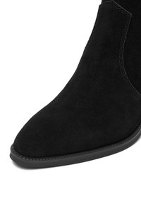 Czarne zamszowe botki kostkowe z szpiczastym noskiem i minimalistycznym designem. Posiadają trwałą czarną gumową podeszwę oraz subtelne akcenty stębnowania.