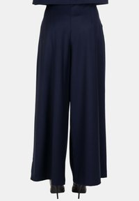 Pantaloni a gamba larga color navy realizzati in materiale morbido, con vita aderente e pieghe sottili, abbinati a scarpe con tacco alto nere.