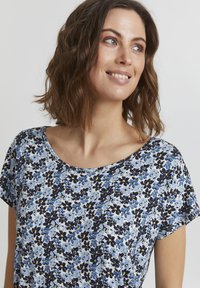 Květinový top s krátkým rukávem s světle modrým pozadím a vzory květin v námořnické modři, žluté a modré; měkká látka s kulatým výstřihem.