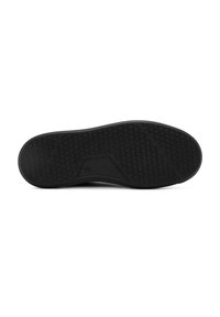 Semelle de chaussure en caoutchouc noir avec un motif de grip texturé, une section centrale lisse et un détail de logo légèrement surélevé.