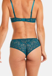 Ensemble de soutien-gorge et de culotte en dentelle teal avec des motifs floraux, des bords festonnés et des bretelles réglables ; la dentelle est semi-transparente.