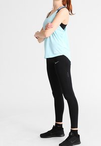 Jasnoniebieski sportowy top na ramiączkach z czarnymi akcentami, w połączeniu z czarnymi legginsami. Top ma luźny krój, a legginsy przylegają do ciała.