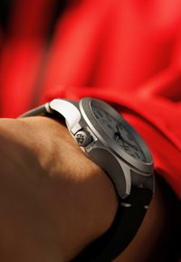 Montre en métal argenté avec un cadran blanc, un bracelet en cuir noir et une couronne texturée. Le design comporte des marqueurs d'heure clairs et deux sous-cadrans.