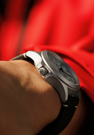 Montre en métal argenté avec un cadran blanc, un bracelet en cuir noir et une couronne texturée. Le design comporte des marqueurs d'heure clairs et deux sous-cadrans.