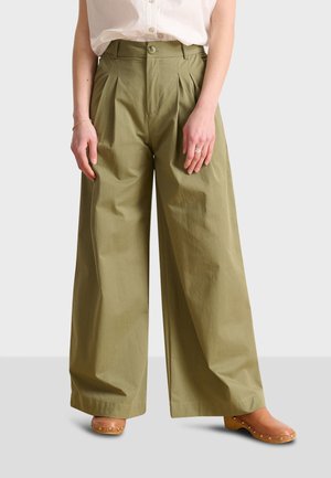 High-waisted, wide-leg pants in olive green cotton with pleats and a button closure, paired with light brown wooden clog sandals.
