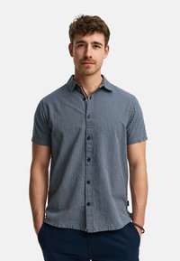 Camisa de manga corta, abotonada, en rayas verticales azul marino y blancas, fabricada en tejido ligero. Presenta un collar abierto y botones oscuros.