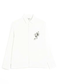 Camicia bianca a maniche lunghe con colletto button-down, caratterizzata da una stampata floreale nera dettagliata sul lato sinistro e una texture liscia.