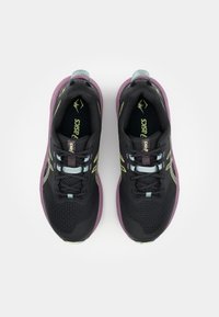 Chaussures de sport noires avec une tige en mesh, semelle violette et accents verts. Elles sont dotées d'un design à lacets et d'un col rembourré pour un confort supplémentaire.