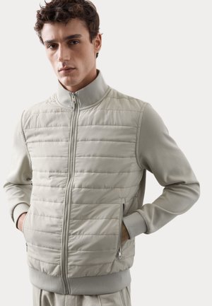 Light gray puffer jacket with zip closure, high collar, ribbed cuffs, and side pockets; features quilted texture and smooth fabric finish.