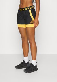 Svarta sportshorts med gula detaljer och ett meshpanel. Funktioner en bred svart midja med texten "ARMOUR UNDER".
