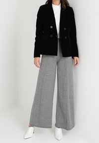 Černý sametový dvouřadý blazer, spárovaný se šedými kalhotami s houndstooth vzorem a bílými muly. Pod ním jednoduchý bílý top.