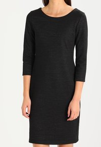 Czarna sukienka do kolan z rękawami o długości trzy czwarte, okrągłym dekoltem i subtelnym, błyszczącym wykończeniem. Gładki materiał i dopasowany krój.
