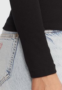 Top nero a maniche lunghe con coste, aderente in vita, abbinato a pantaloncini di jeans azzurri con una toppa sulla tasca posteriore e cuciture visibili.