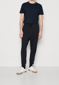 Mörkblå kortärmad skjorta med en diskret logotyp, kombinerad med svarta smala joggers, avslutad med vita sneakers och svarta ankelsockor.