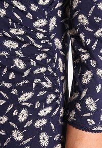 Marinfärgad tyg med vitt parasollmönster, med rynkad detalj och vågig nederkant på ärmen. Mjuk textur, figurnära design.